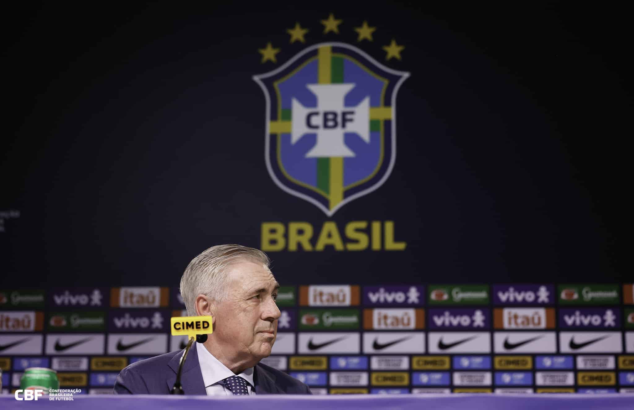 Técnico Carlo Ancelotti olha para o lado com o escudo da CBF ao fundo