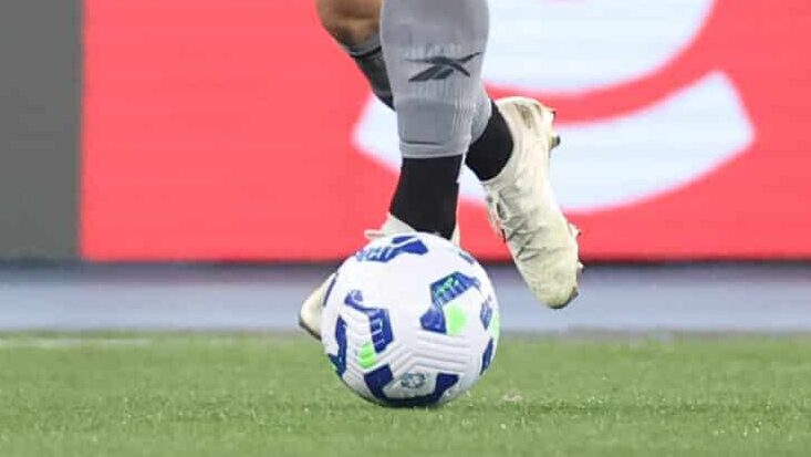 Pés do jogador conduzem bola no gramado